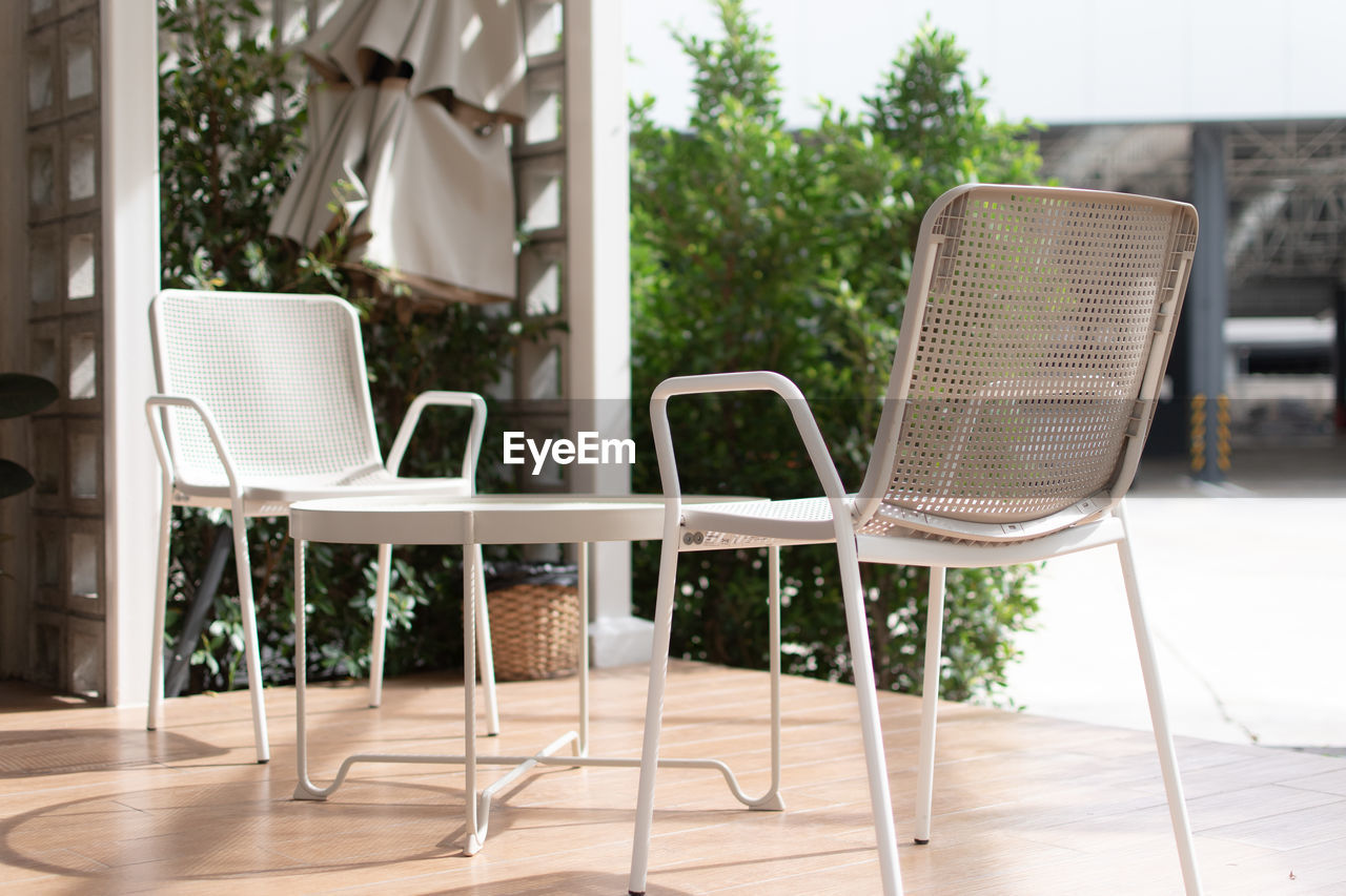 EMPTY CHAIRS AND TABLE BY WINDOW IN YARD