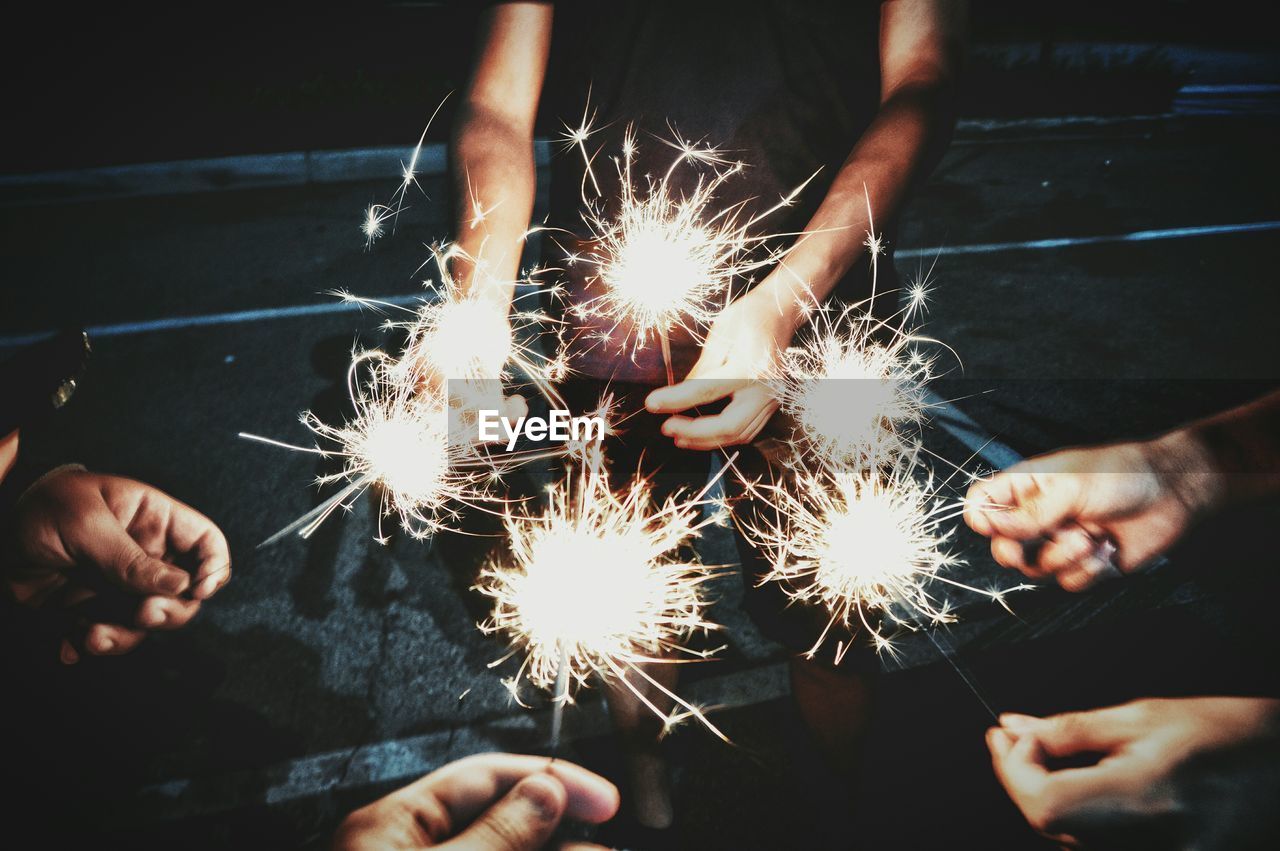 Cropped image of people holding sparklers while standing outdoors at night