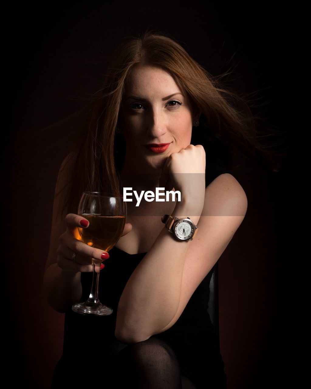 Portrait of young woman holding wineglass while sitting against black background