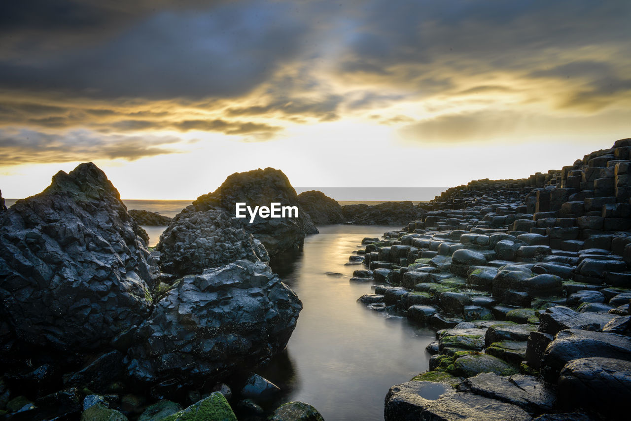 Rocks in sea against sky during sunset
