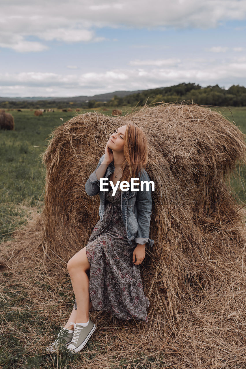 Full length of woman sitting by hay stack