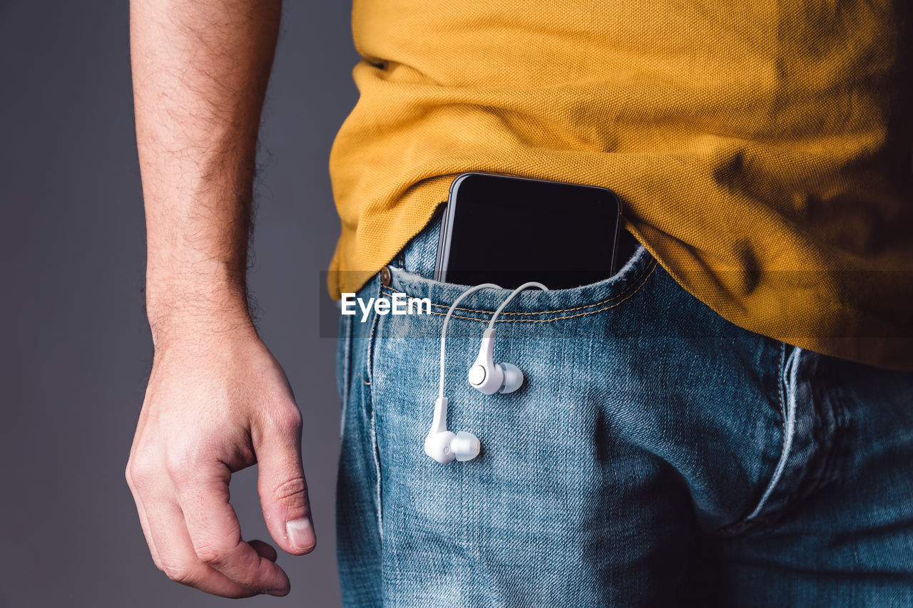 Midsection of man with mobile phone and in-ear headphones in pocket