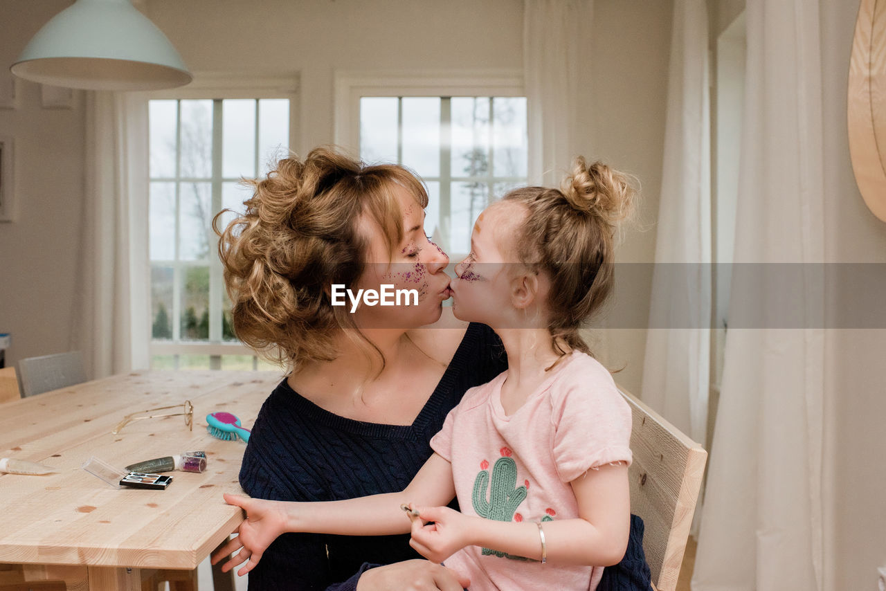 Mother kissing daughter whilst they play with make up at home