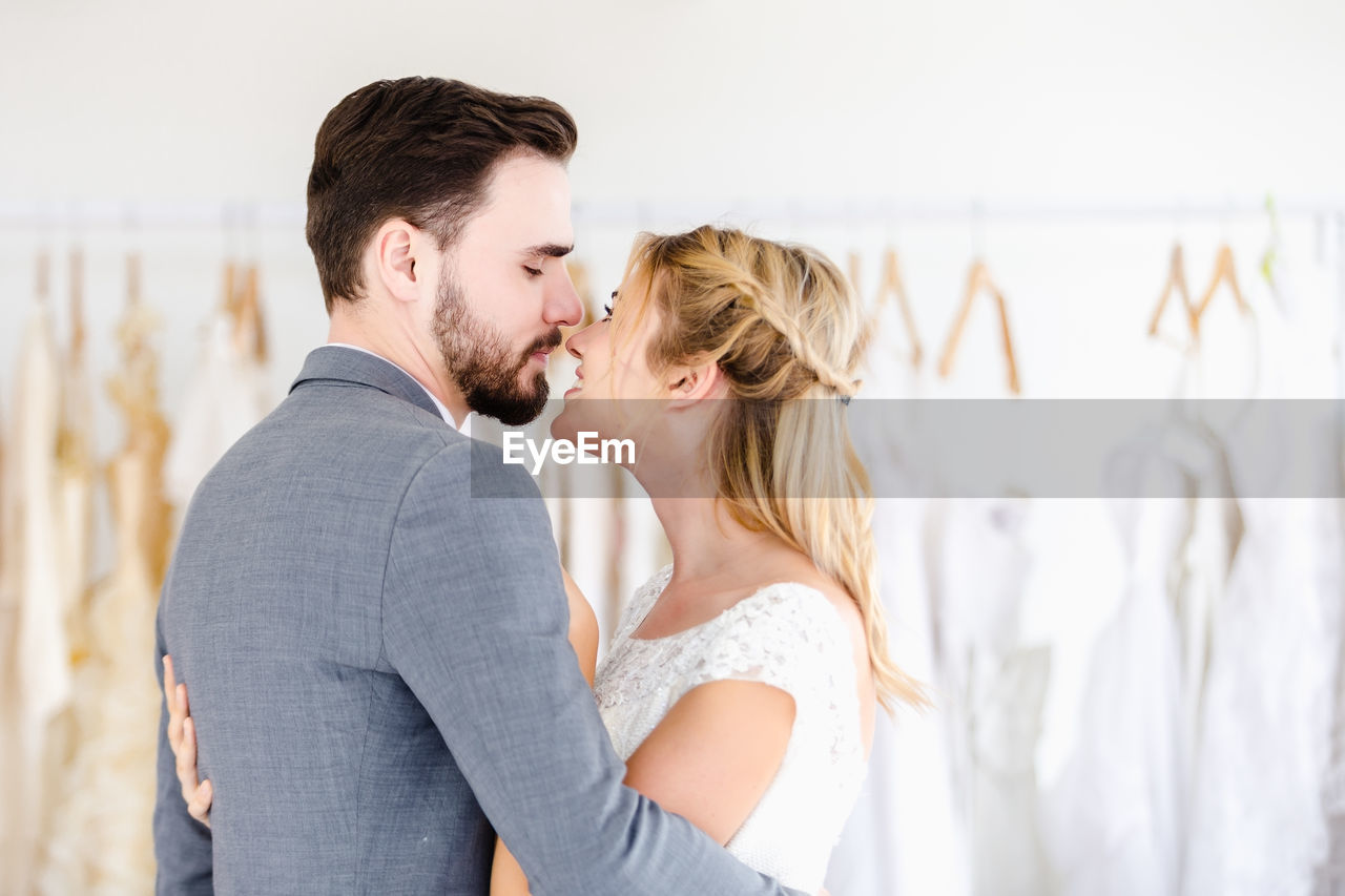 Bride and groom embracing while standing in boutique