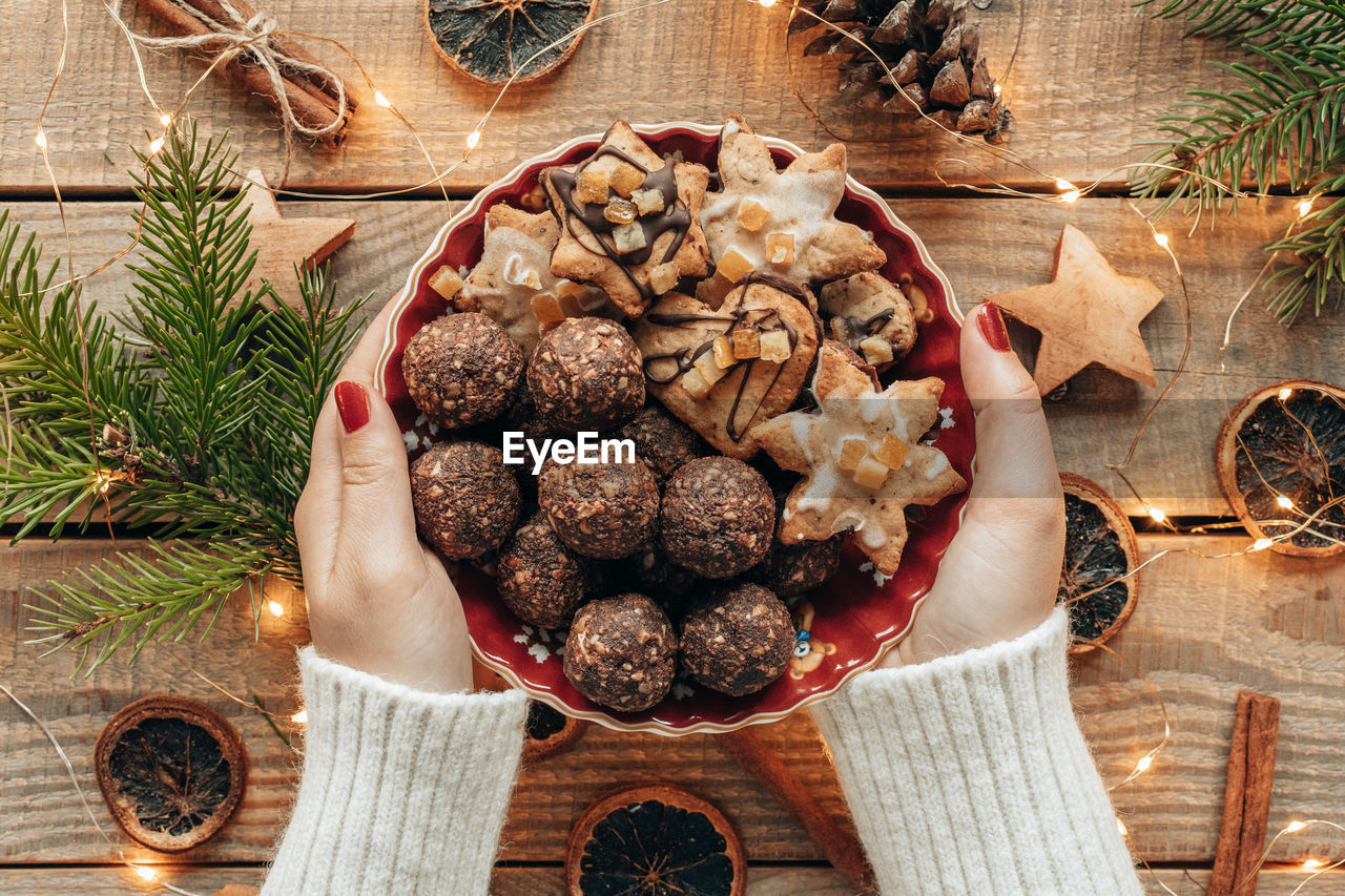 Overhead photo of hands holding plate of christmas cookies over wooden boards with decorations