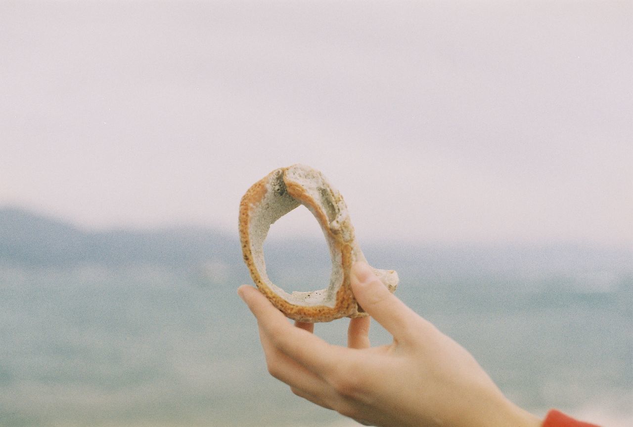 Close-up of a hand holding stone against blurred sea