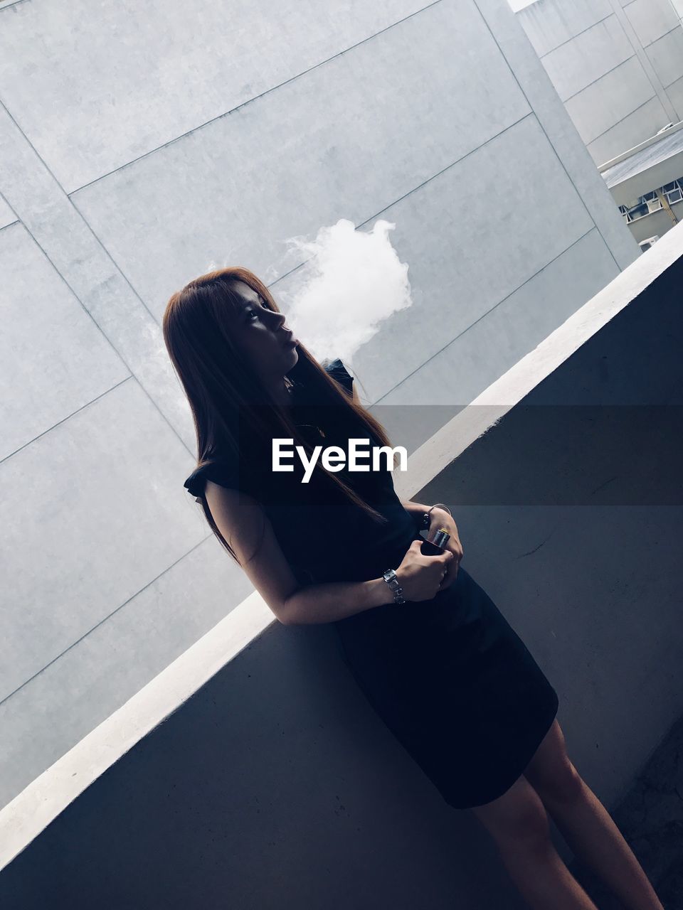 Tilt shot of woman smoking while standing against building