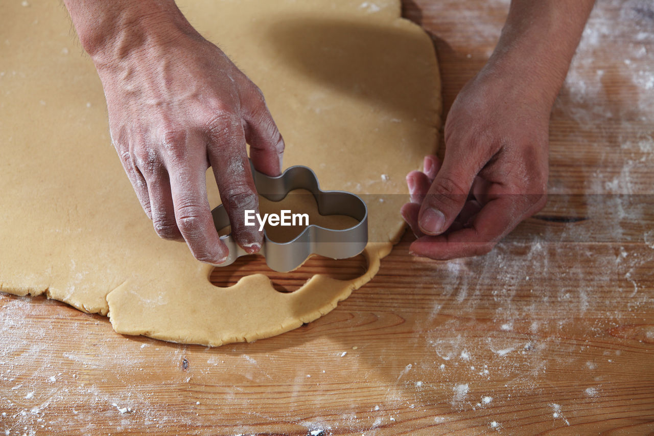 Cropped hands of chef cutting dough with pastry cutter at table