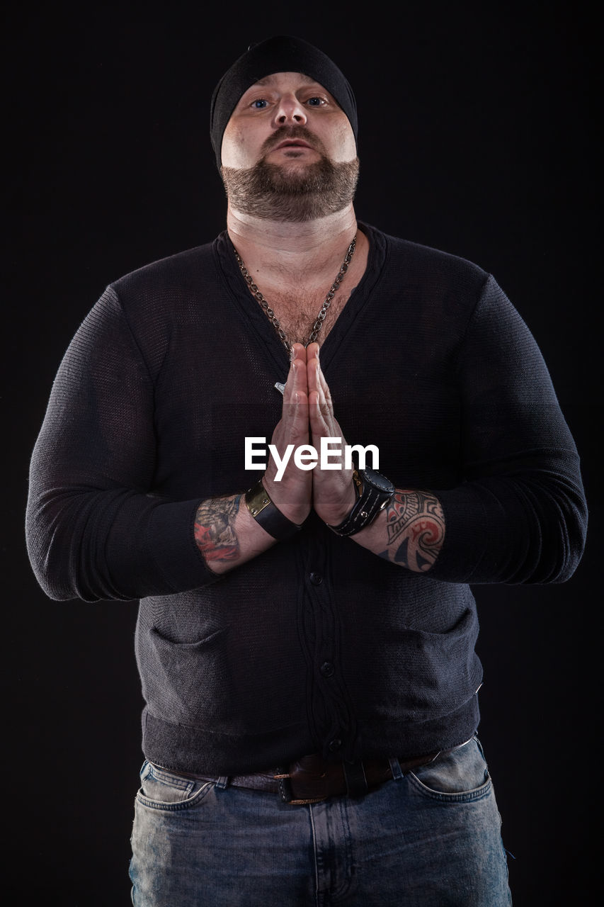 Portrait of hipster man with hands clasped standing against black background