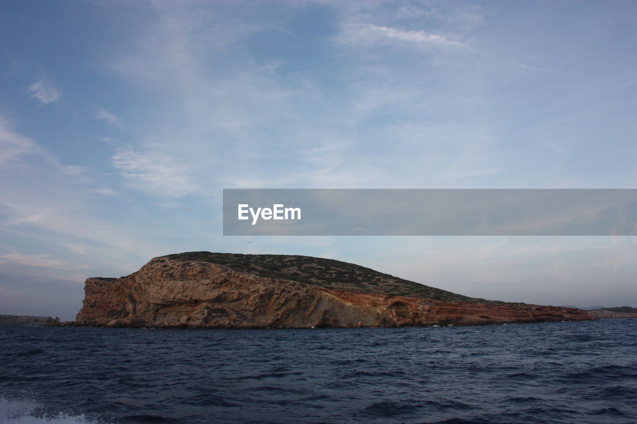 Islet or rocky cliff between the rough sea of ibiza and the blue sky in balearic islands