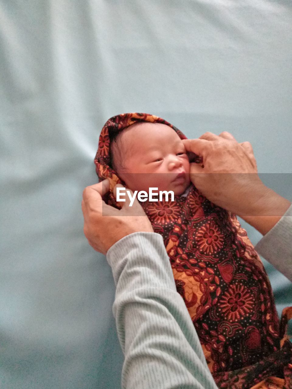 Cropped hands of person wrapping cute baby boy lying on bed at home