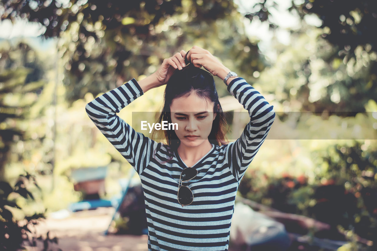 Woman tying hair while standing against tree