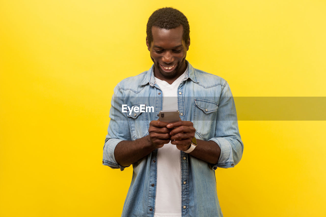 Man holding camera while standing against yellow background