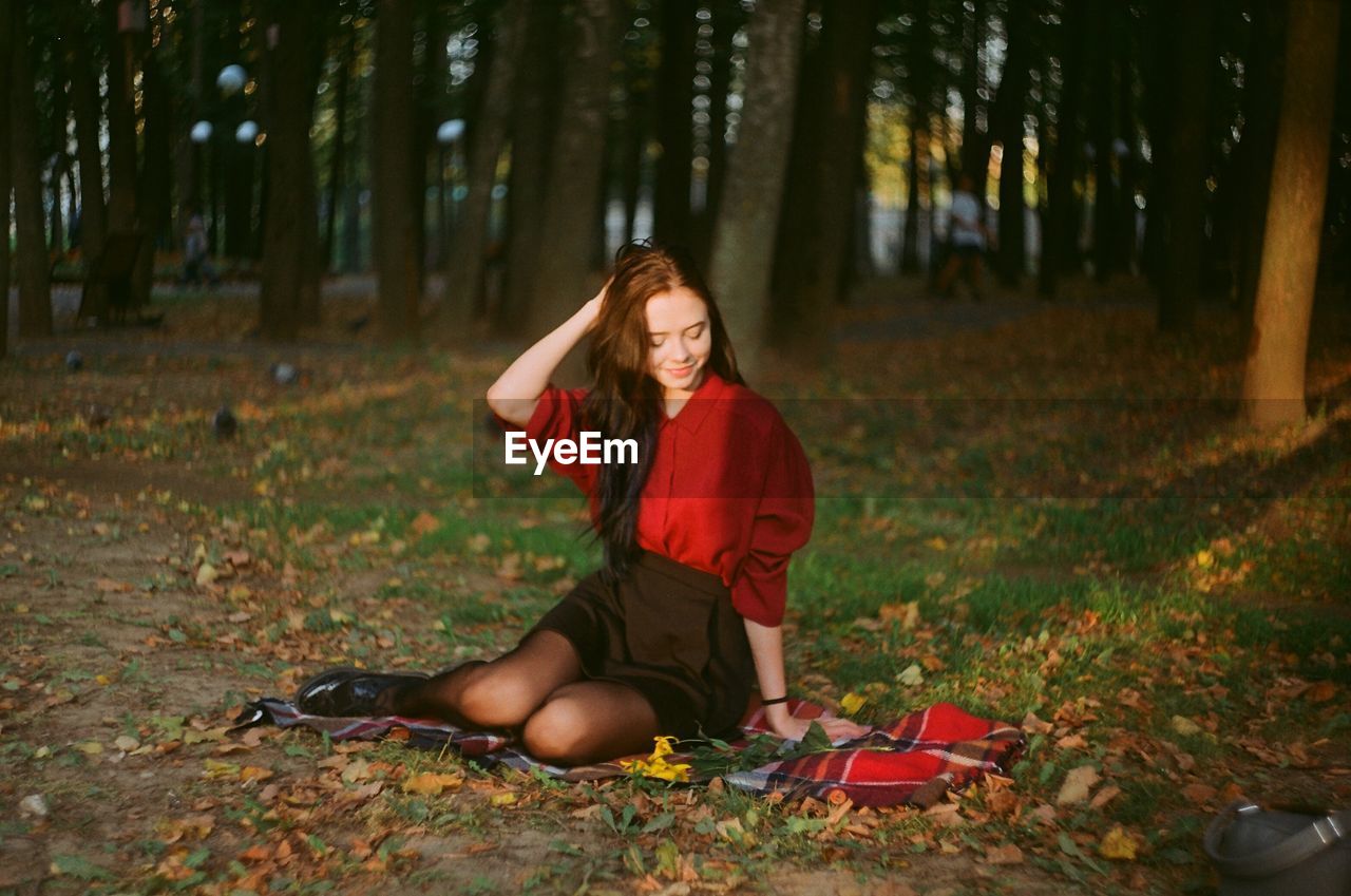 Smiling young woman sitting in forest during autumn