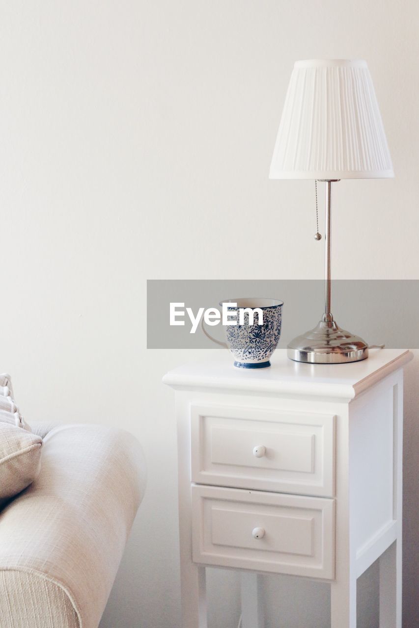 Cup and lamp shade on side table against wall at home