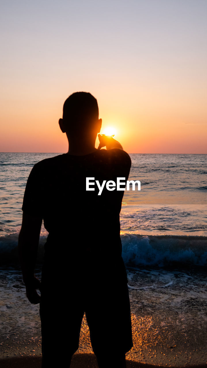 Vertical shot of a silhouette of a man pointing at the sun during sunset