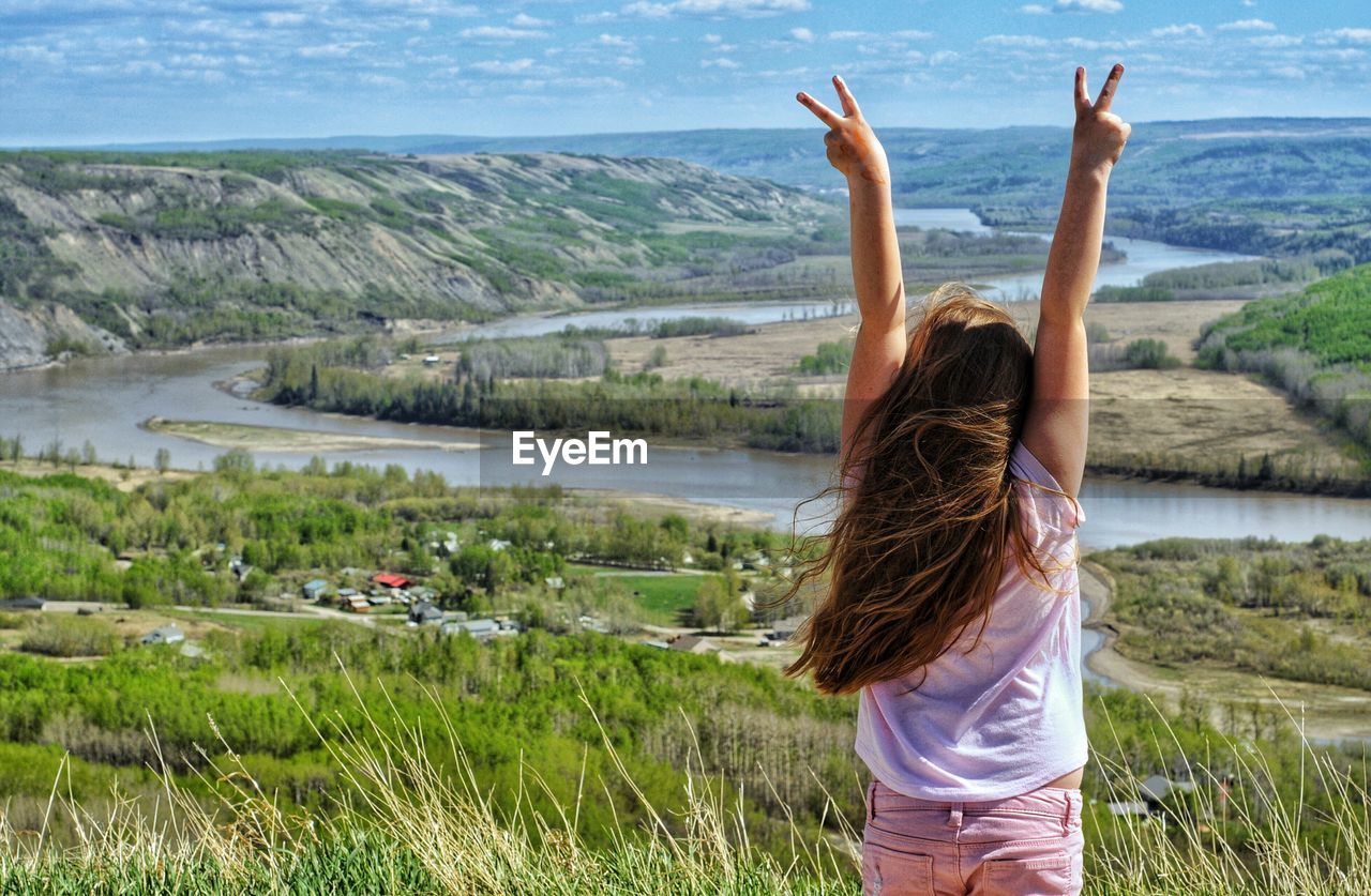 Rear view of woman with hands raised gesturing peace sign against landscape