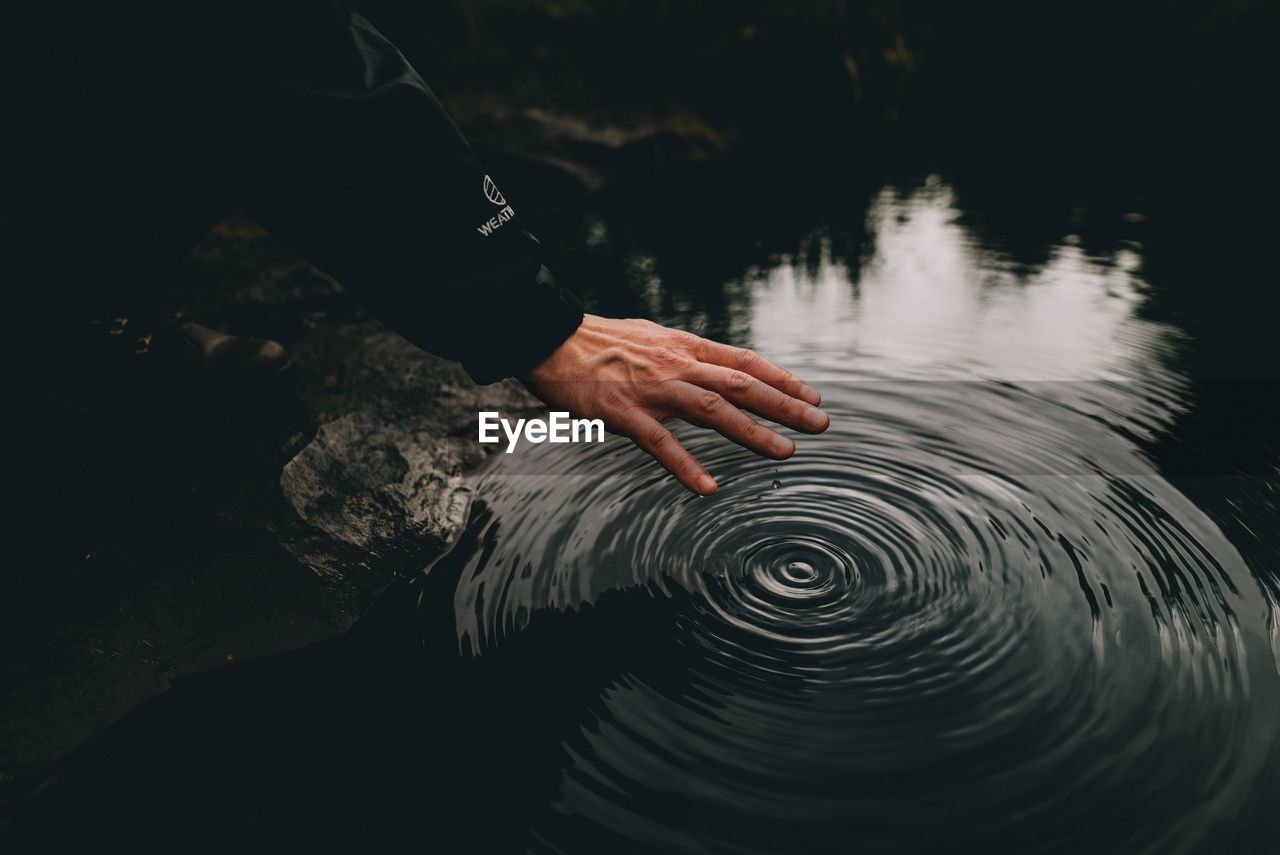 Cropped image of hand over rippled water in lake