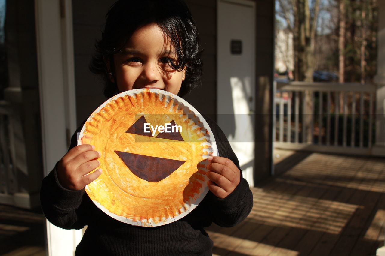 Portrait of girl holding smiley face artwork at porch