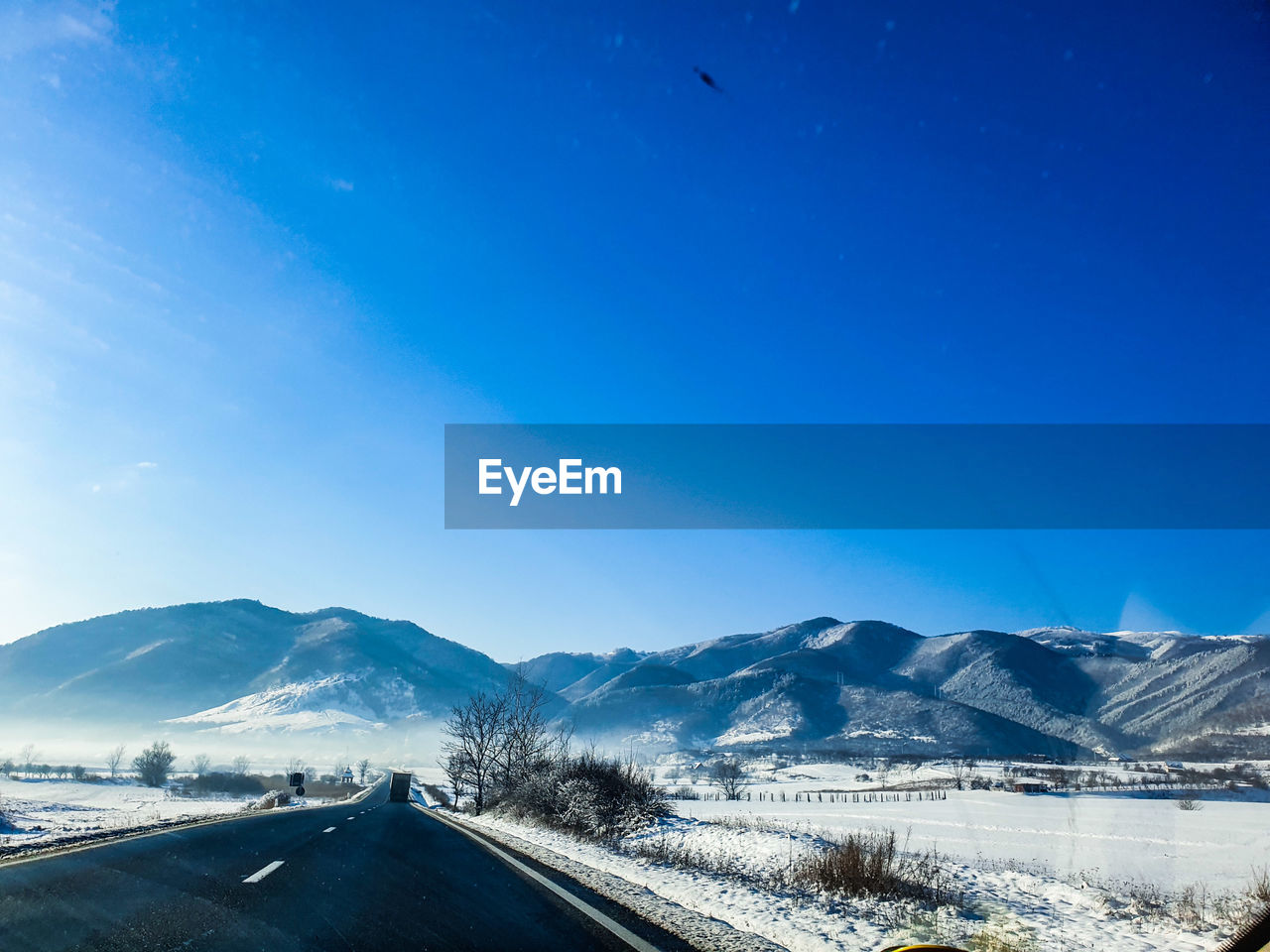 Road by snowcapped mountains against blue sky