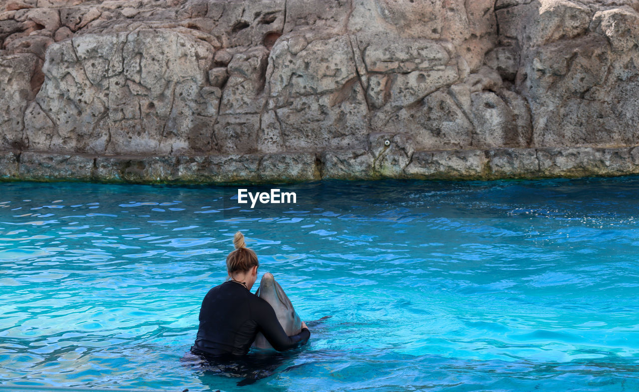 WOMAN SITTING ON ROCK IN SEA