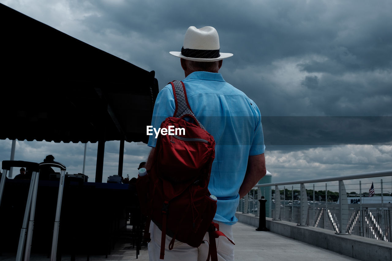 Rear view of man on pier against cloudy sky