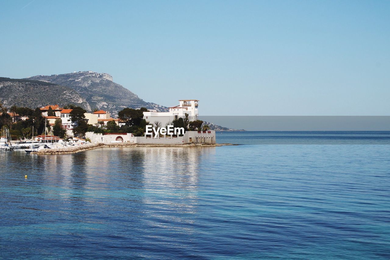 Scenic view of river by buildings against clear blue sky