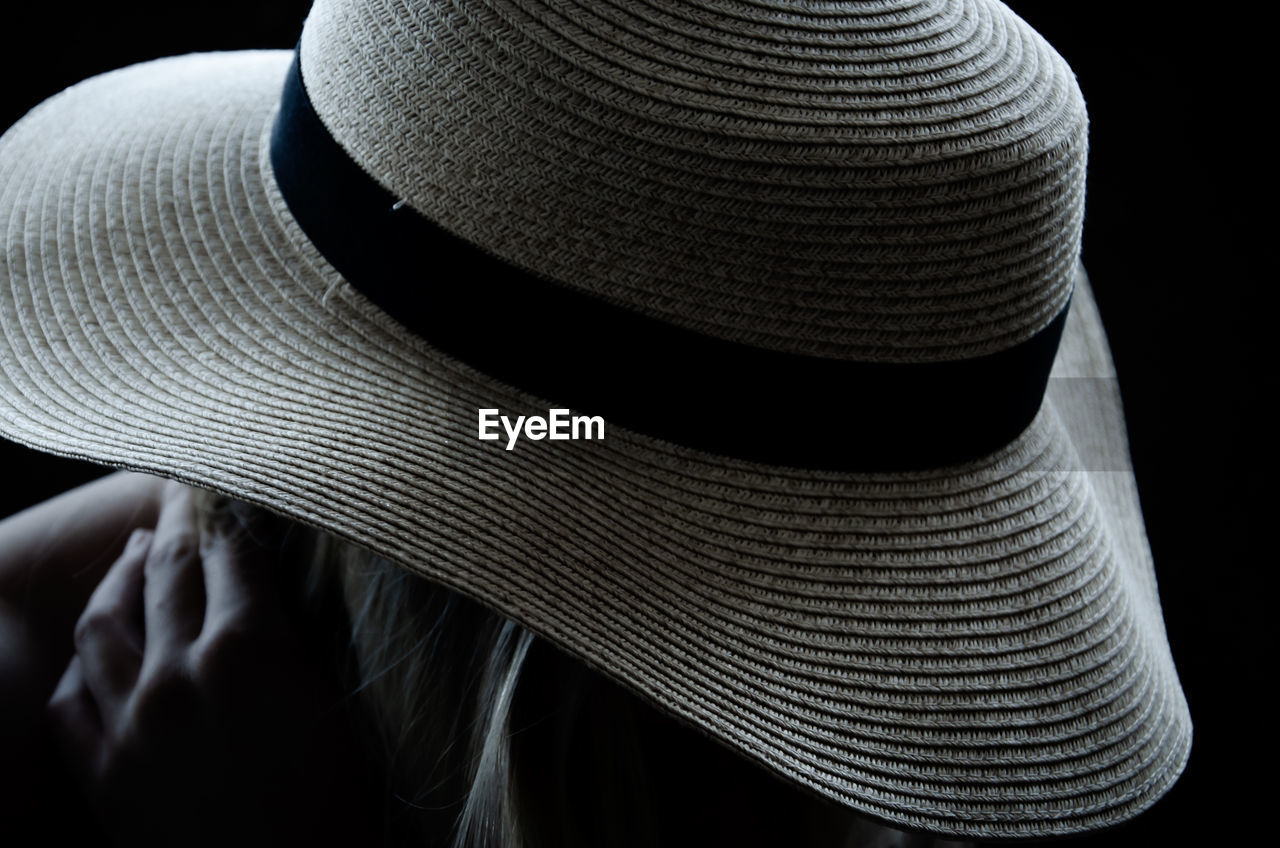 Close-up of person wearing hat against black background