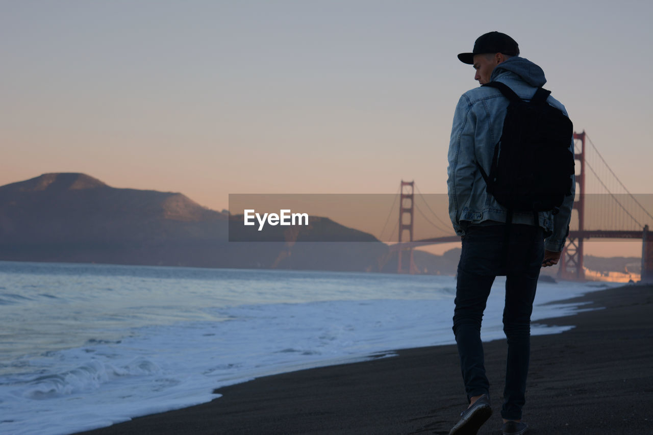 Rear view of man walking against golden gate bridge during sunset