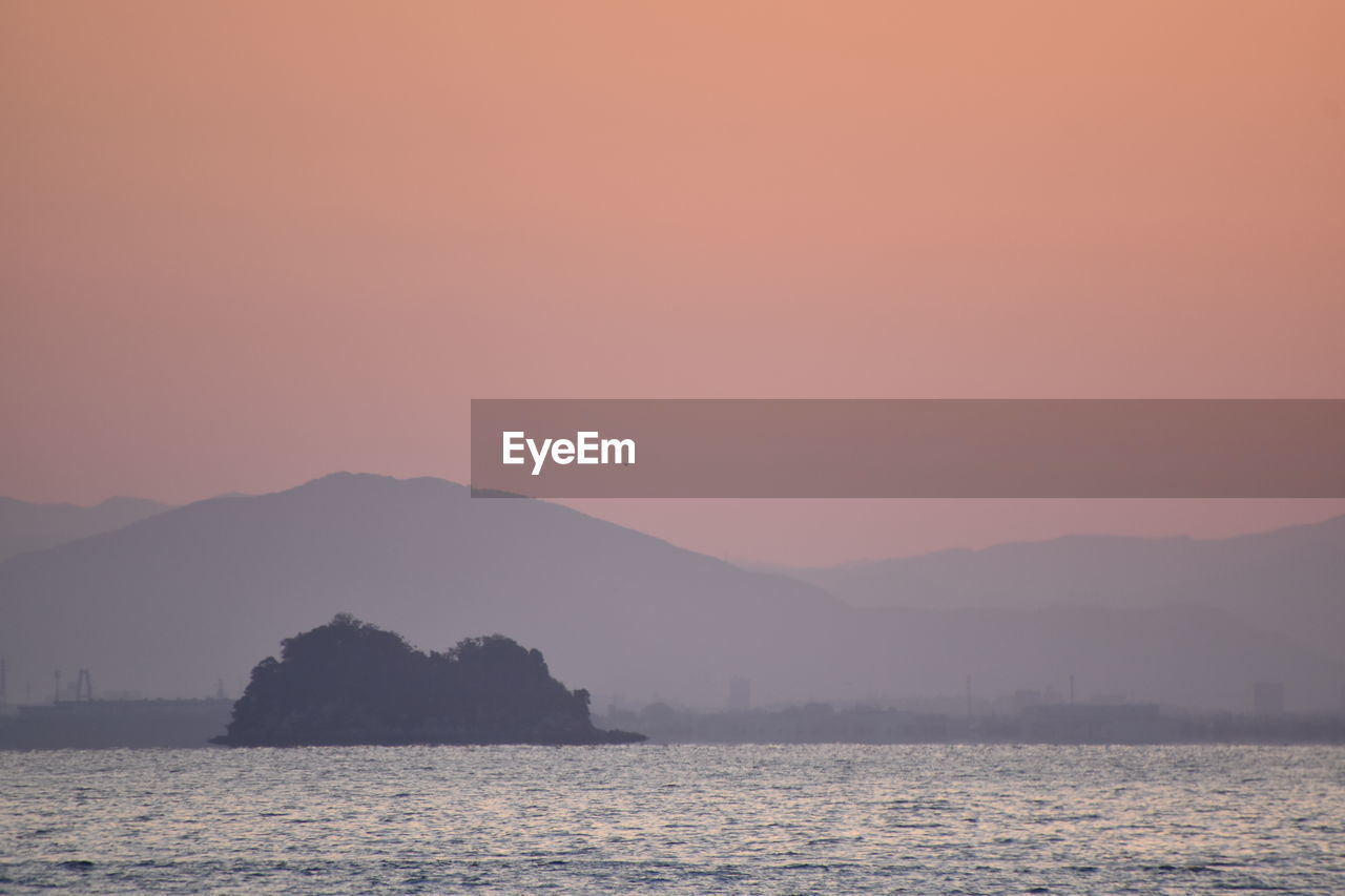 SCENIC VIEW OF SEA AND SILHOUETTE MOUNTAINS AGAINST ORANGE SKY