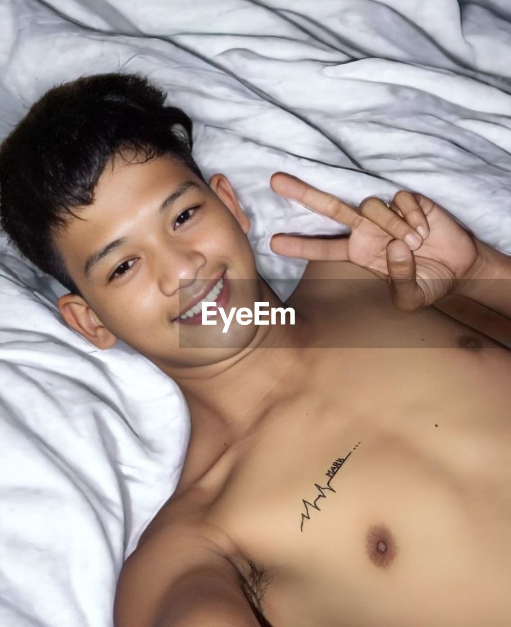 bed, lying down, relaxation, furniture, indoors, bedroom, adult, portrait, smiling, person, one person, domestic room, young adult, black hair, skin, human face, human mouth, high angle view, limb, looking at camera, human leg, hand, lifestyles, women, emotion, happiness, men, waist up, close-up, arm, human hair, positive emotion, lying on back, cheerful, resting, sheet, female, nose, headshot, directly above, comfortable