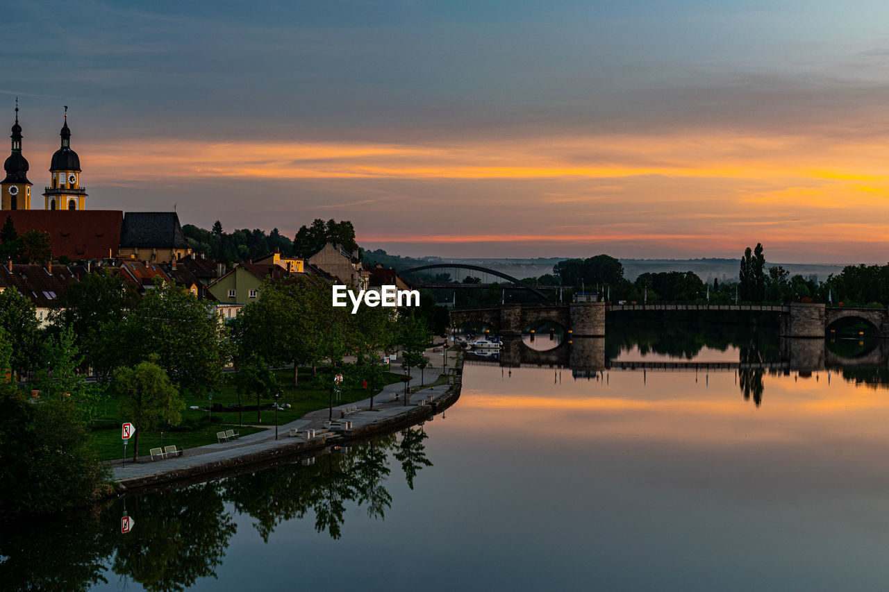 SCENIC VIEW OF RIVER BY BUILDINGS AGAINST SKY AT SUNSET