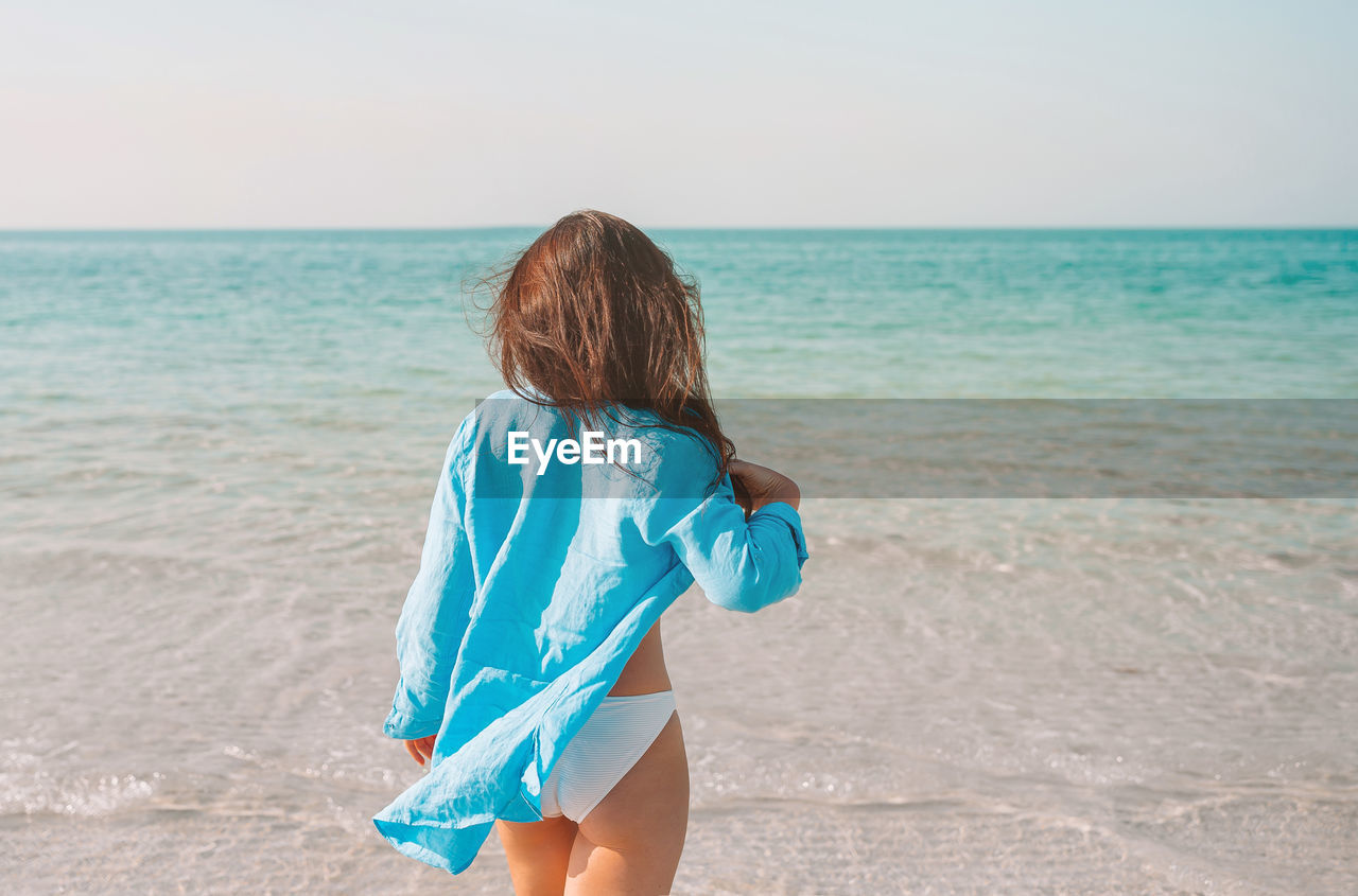 Rear view of boy standing on beach against sky