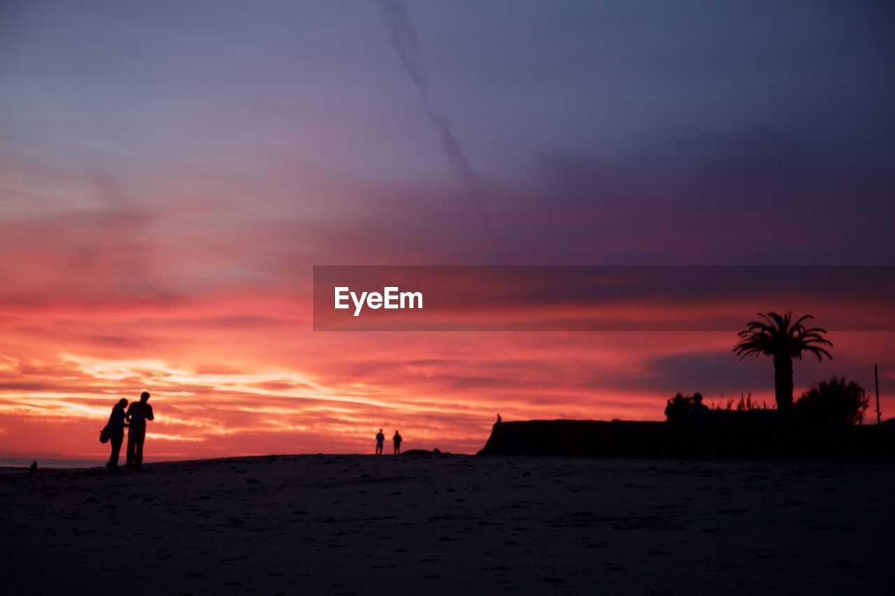 Silhouette of people on beach against cloudy sky