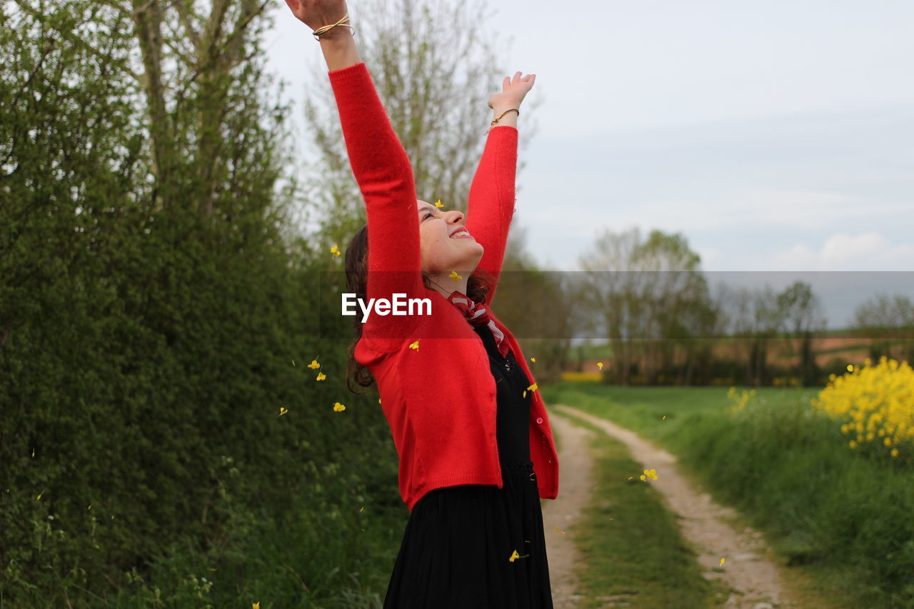 Smiling woman standing with arms raised against plants