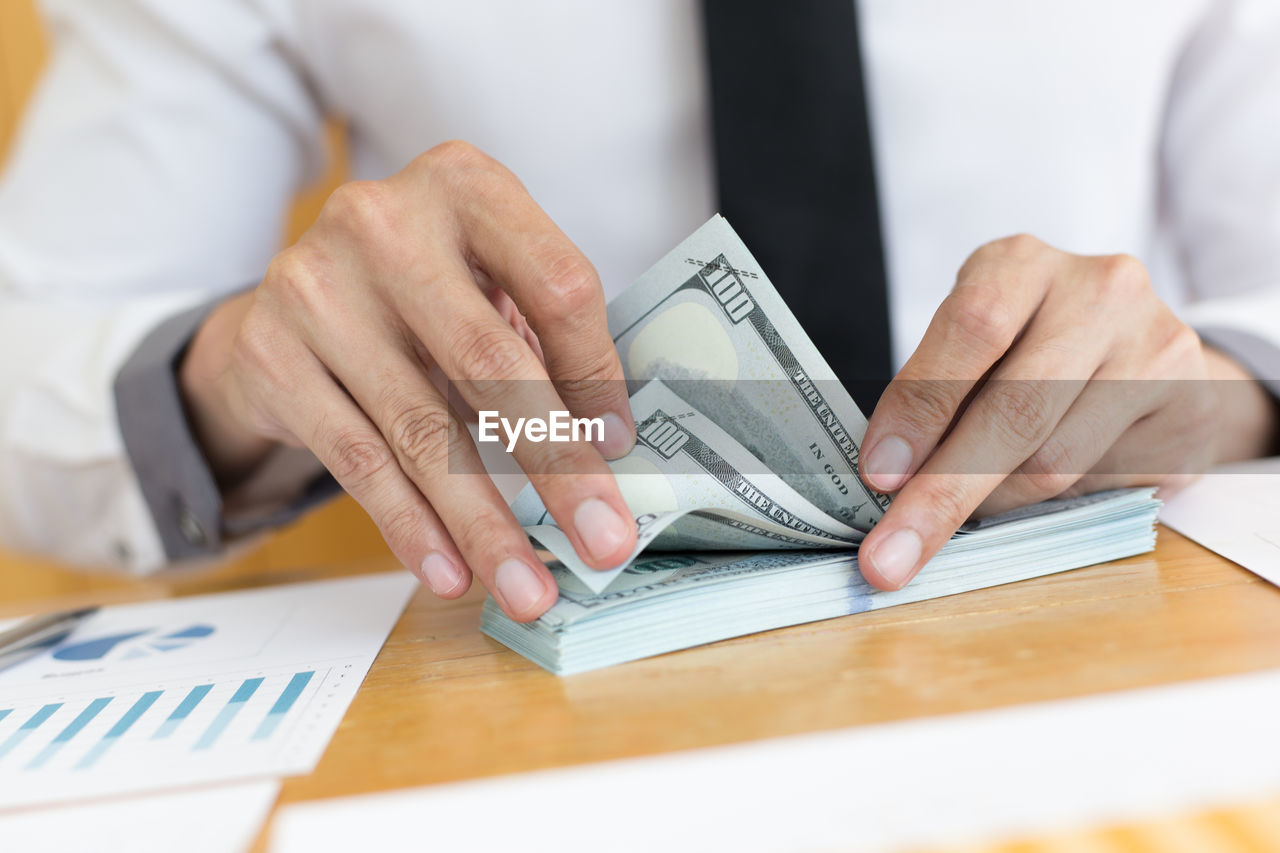 Midsection of businessman counting paper currency on desk