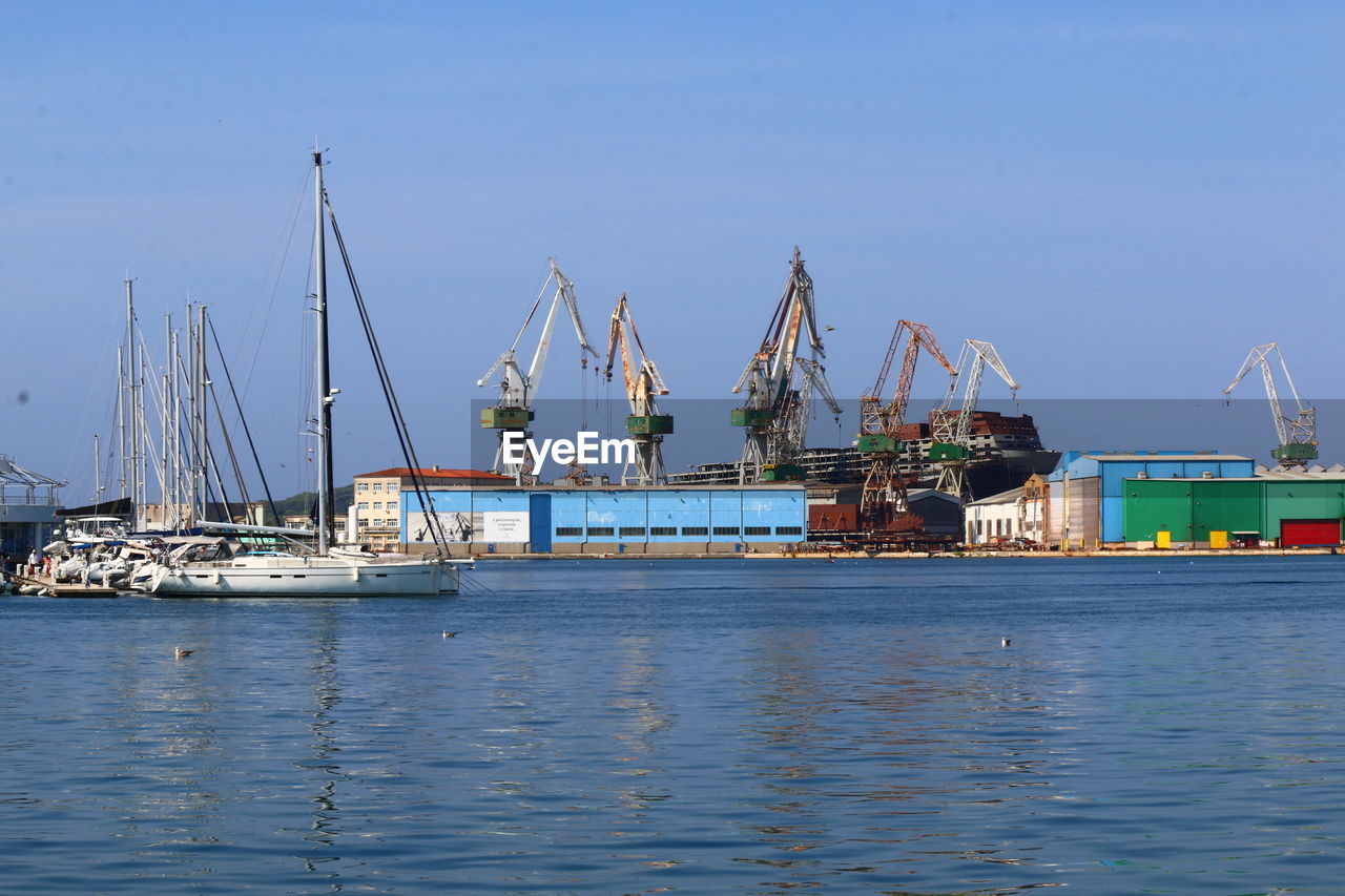 Shipyard and boats in sea against clear sky