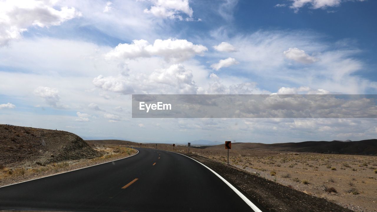 Road passing through landscape against cloudy sky