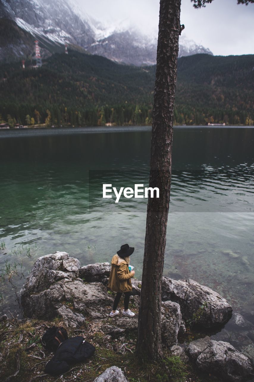 High angle view of woman standing on rock by lake against sky