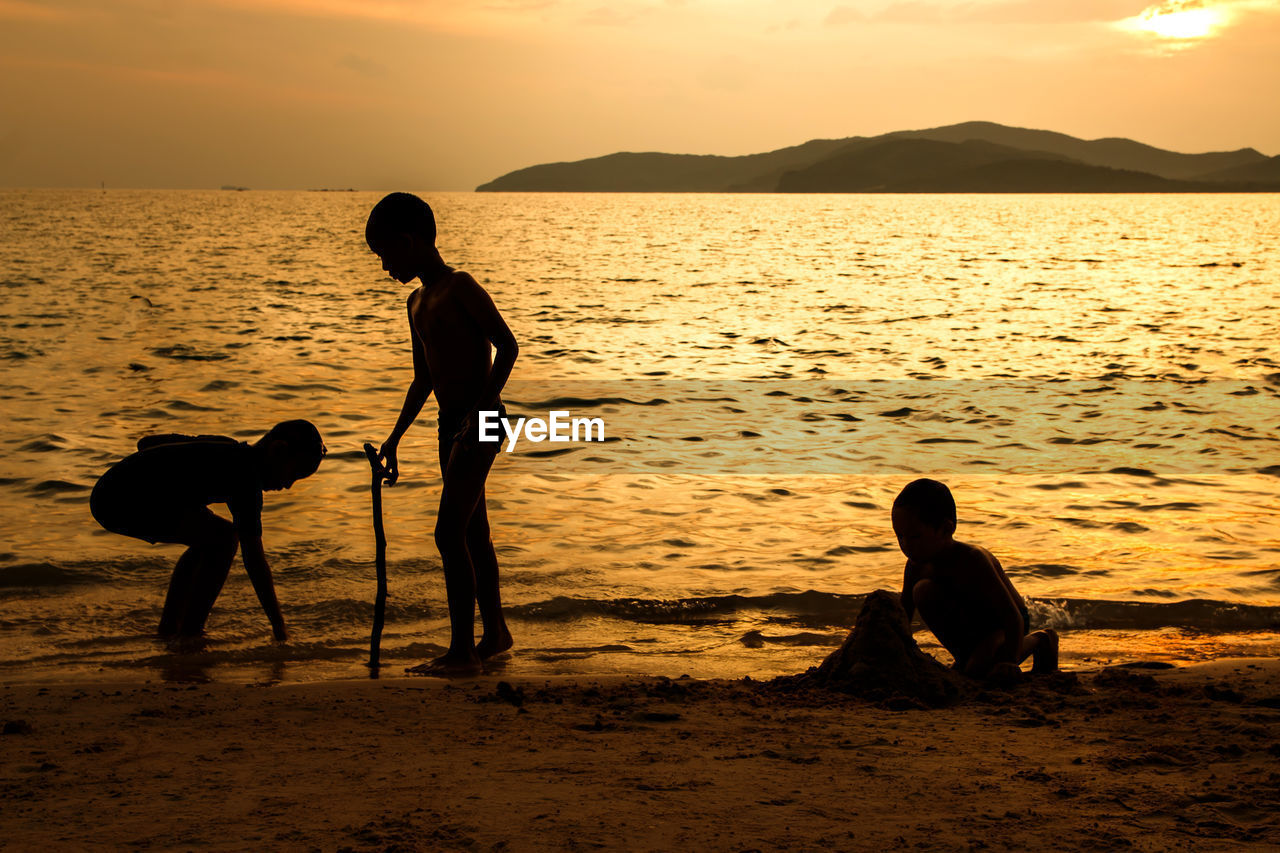 SILHOUETTE MEN PLAYING AT BEACH DURING SUNSET