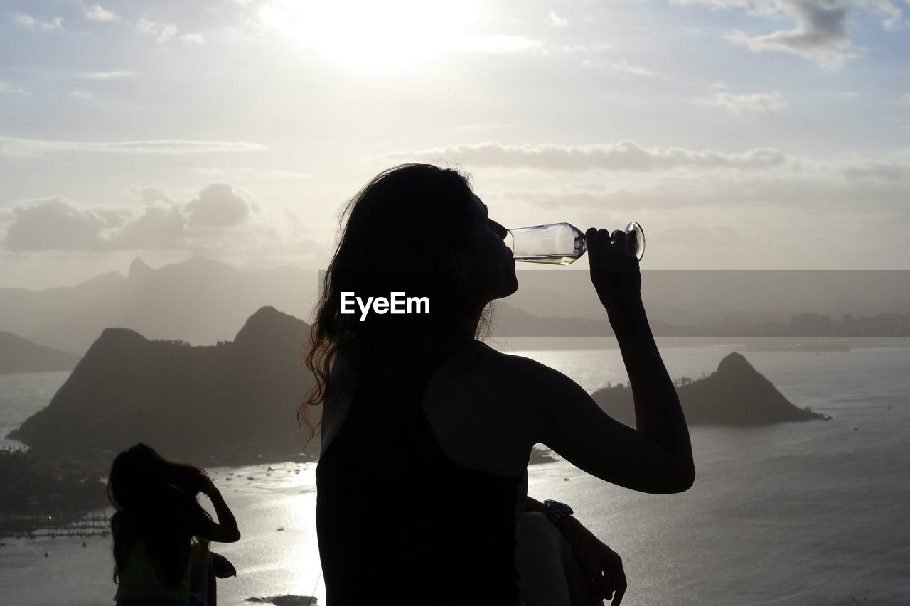 Silhouette two women drinking wine on mountain by sea during sunset