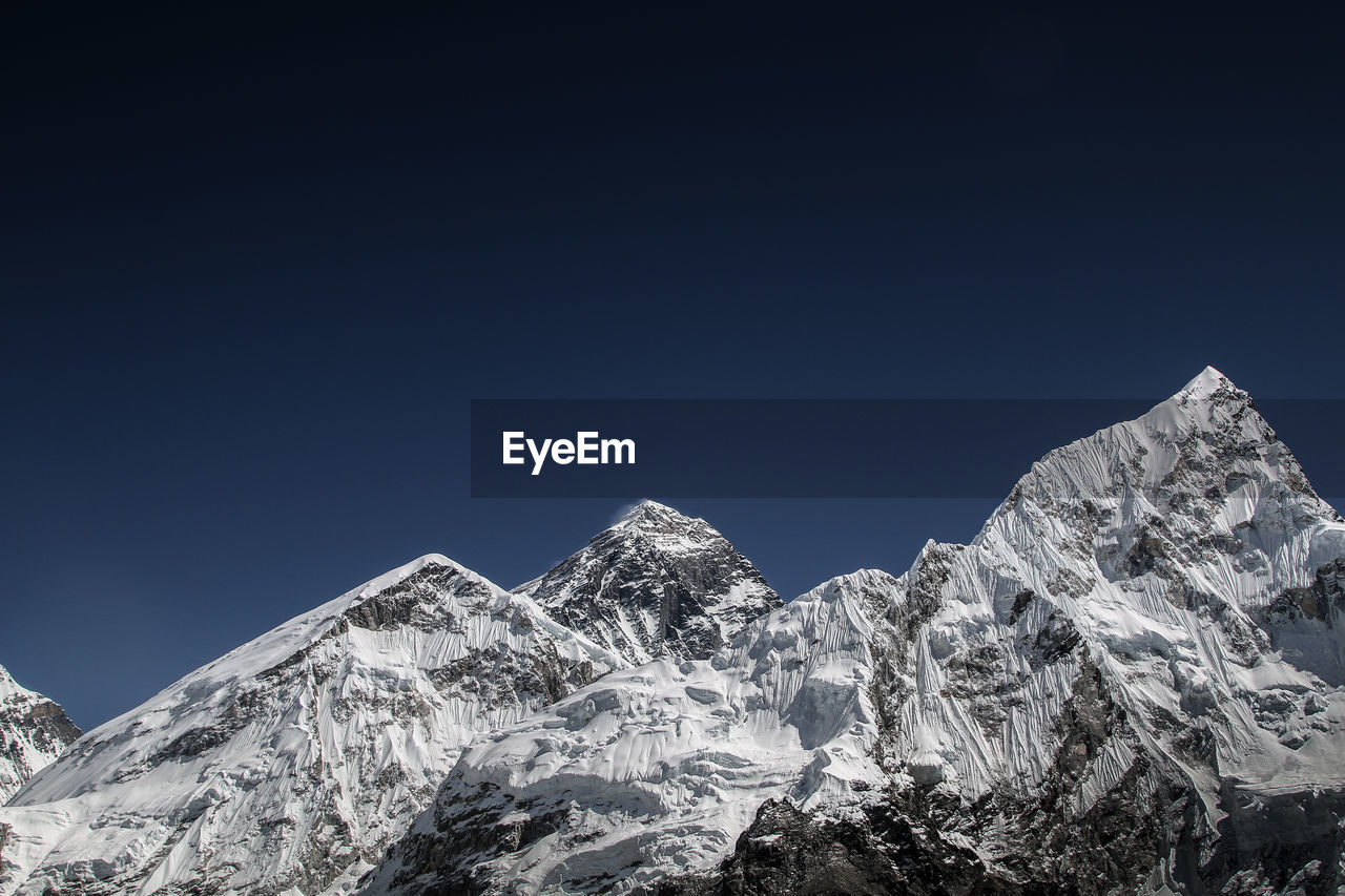 Low angle view of snowcapped mountains against clear blue sky