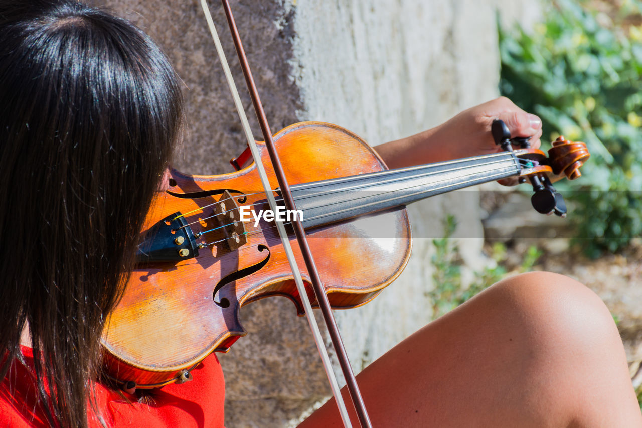 Close-up of woman playing violin while sitting outdoors