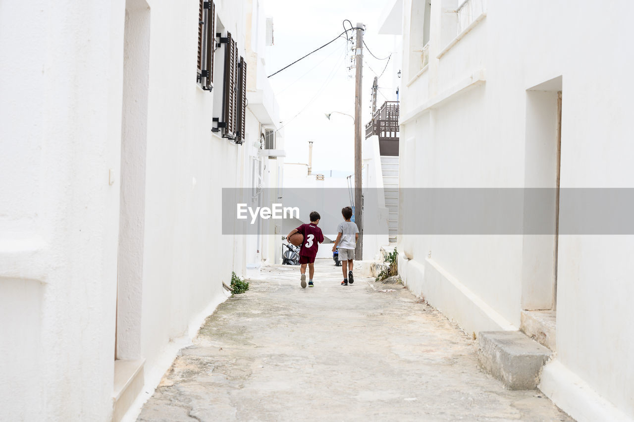 PEOPLE WALKING ON ALLEY AMIDST BUILDINGS