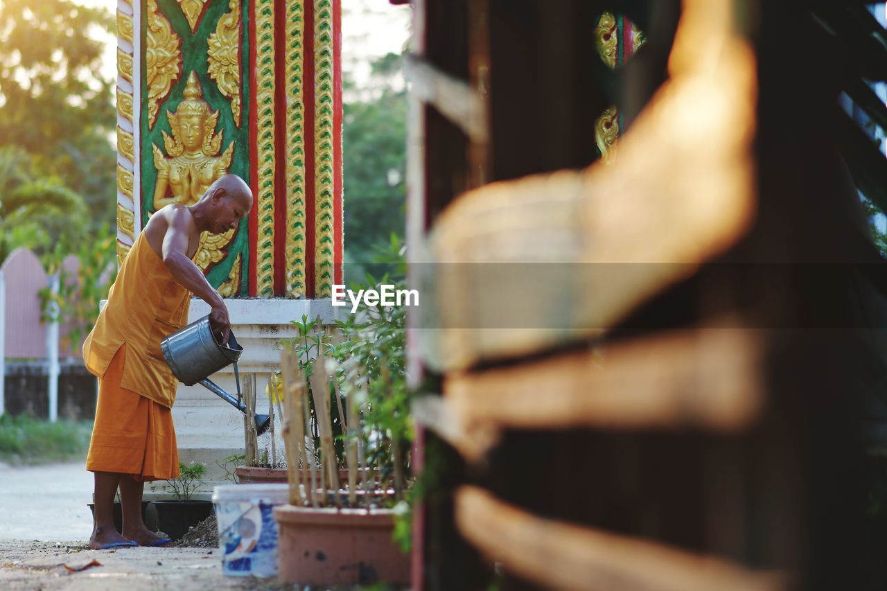 Side view of monk watering plants at temple