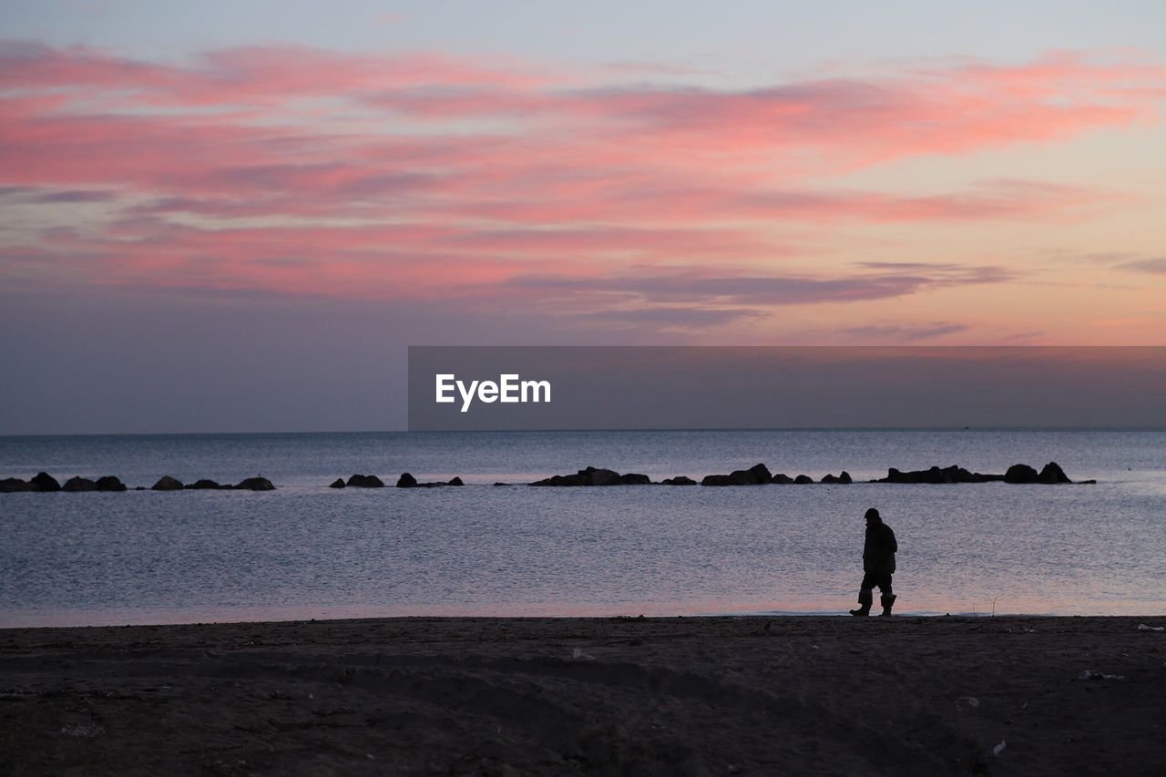 Silhouette man standing at beach against sky during sunset