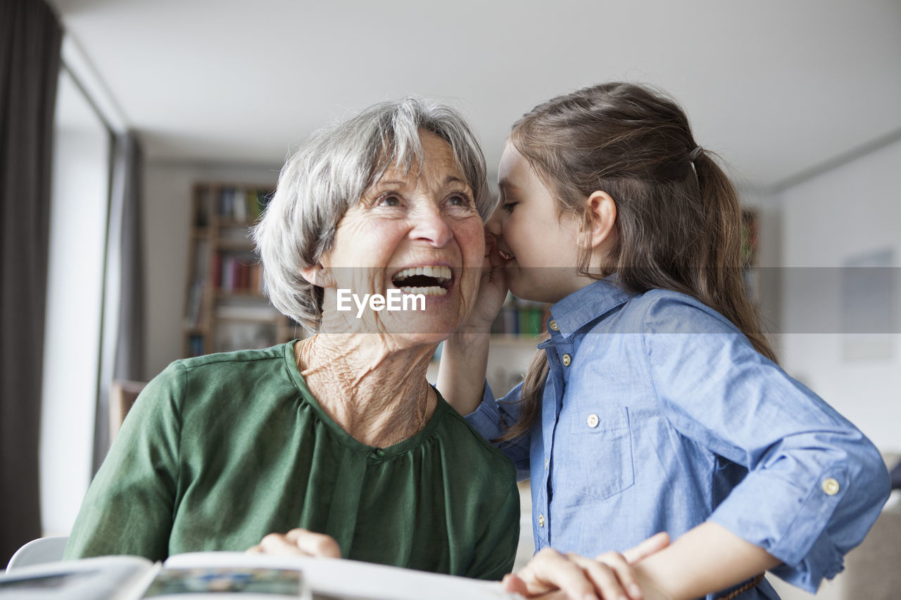 Granddaughter wispering something in the ear of her grandmother