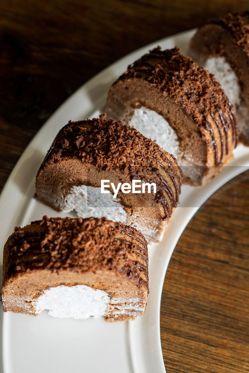 Chocolate roll with fresh cream on a white plate and wooden background