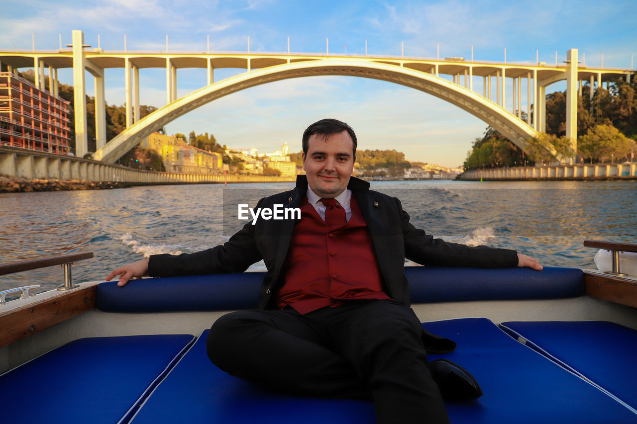 Portrait of smiling groom sitting in boat against bridge over sea