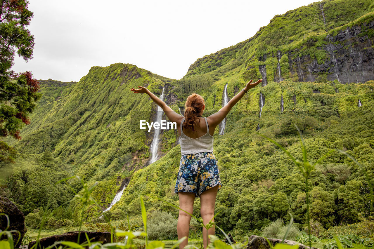 Woman in green vegetation, view to waterfall, at flores island, azores travel destination.